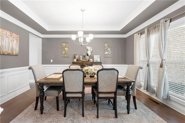 dining space with an inviting chandelier, visible vents, a tray ceiling, and wood finished floors