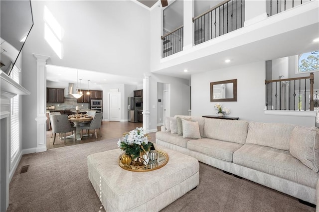 carpeted living area featuring a fireplace, a towering ceiling, decorative columns, and baseboards