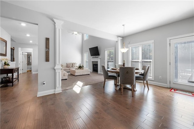 dining space with dark wood finished floors, a glass covered fireplace, decorative columns, and baseboards