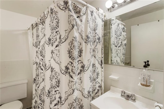 bathroom with tile walls, curtained shower, toilet, wainscoting, and vanity