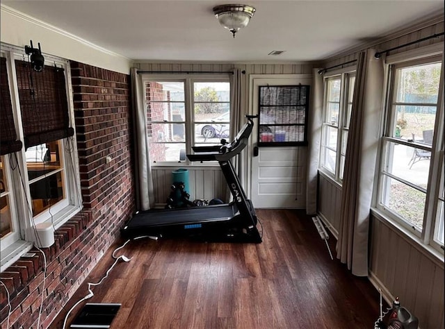 exercise room with visible vents, brick wall, and wood finished floors