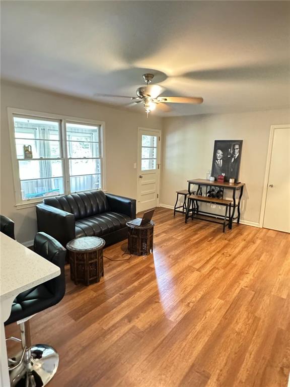 living area featuring baseboards, light wood-style floors, and a ceiling fan