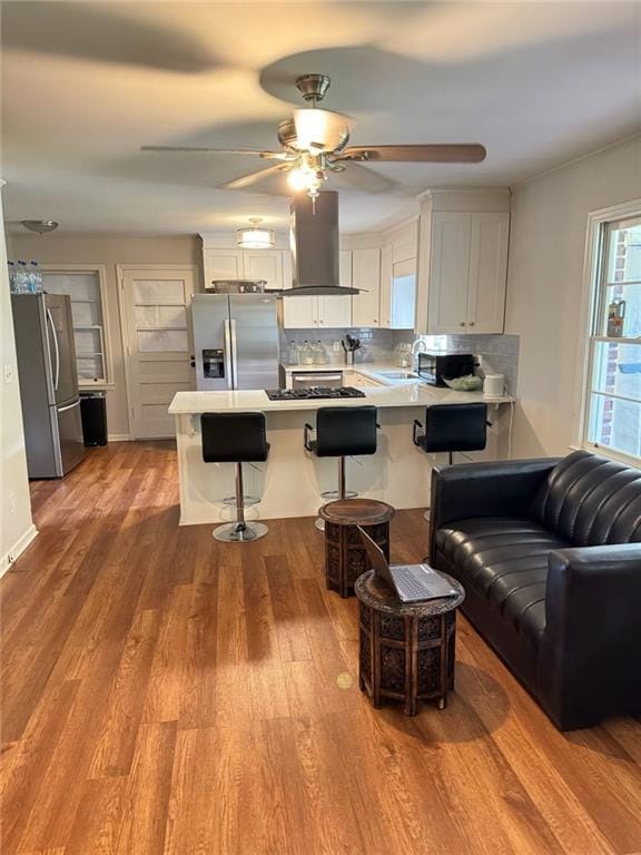 kitchen with wood finished floors, a peninsula, stainless steel fridge with ice dispenser, freestanding refrigerator, and island range hood