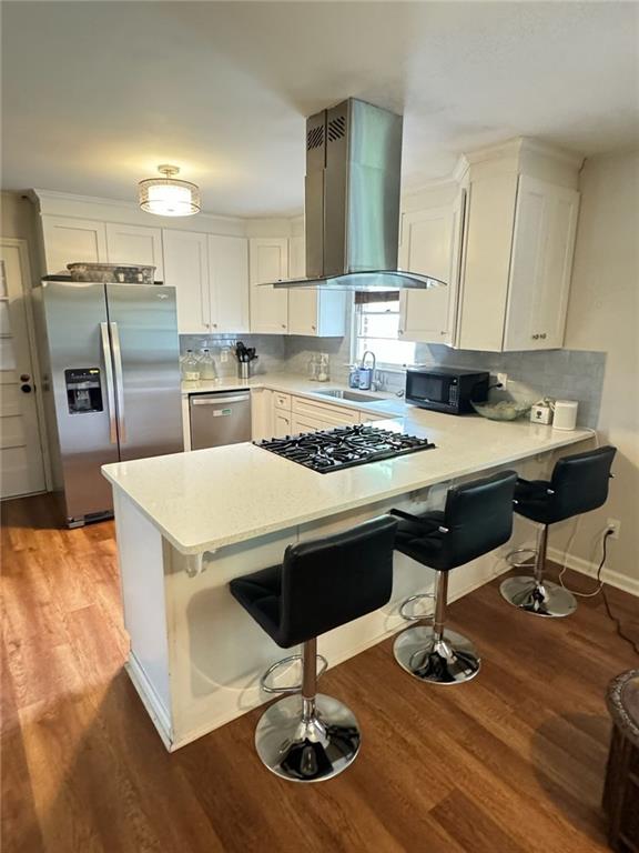 kitchen featuring ventilation hood, light countertops, a peninsula, black appliances, and a sink