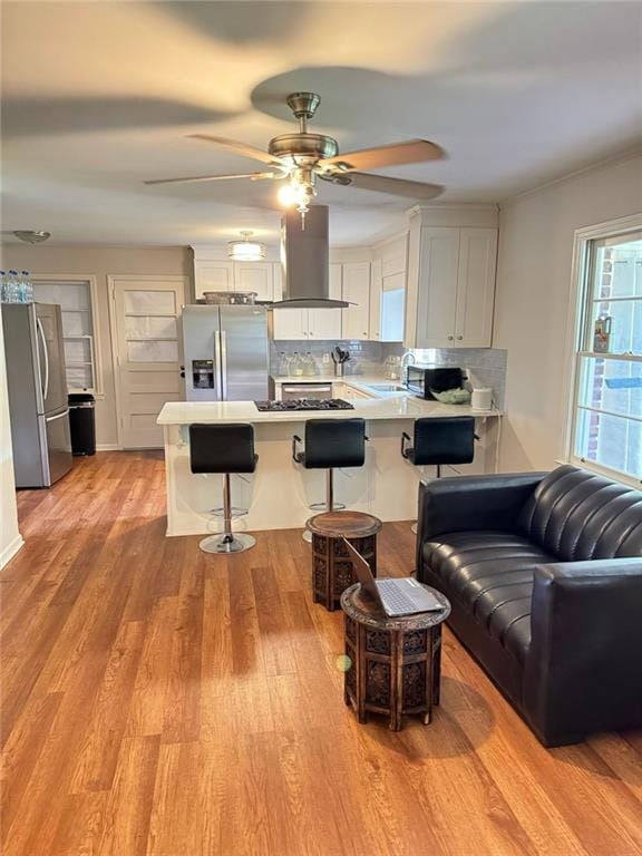 kitchen with a breakfast bar area, a peninsula, island exhaust hood, freestanding refrigerator, and stainless steel fridge