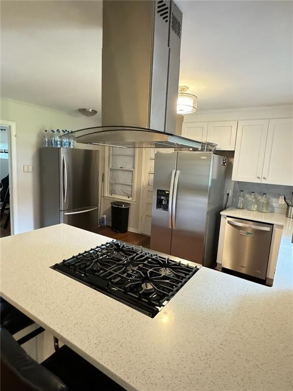 kitchen featuring backsplash, light stone counters, island exhaust hood, white cabinets, and stainless steel appliances