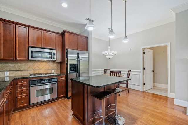 kitchen with light wood-type flooring, dark stone counters, stainless steel appliances, crown molding, and pendant lighting