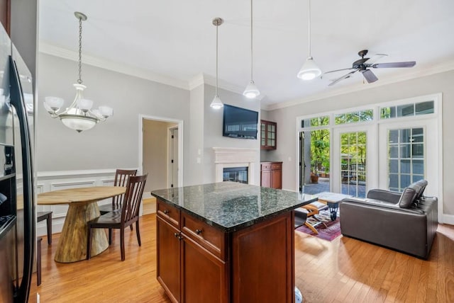 kitchen featuring hanging light fixtures, dark stone counters, light hardwood / wood-style floors, a kitchen island, and ceiling fan with notable chandelier