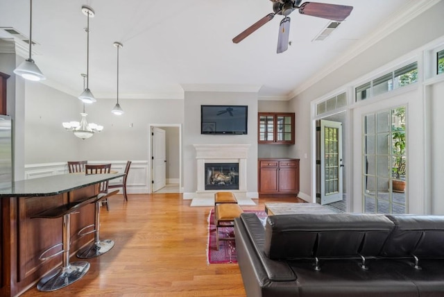 living room with ceiling fan with notable chandelier, light hardwood / wood-style floors, and ornamental molding