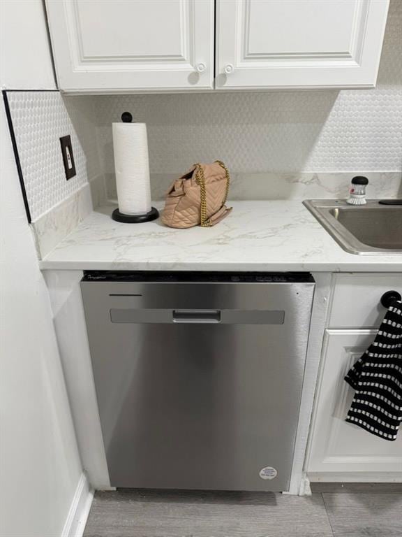 interior details with light stone countertops, light wood-type flooring, white cabinets, sink, and dishwasher