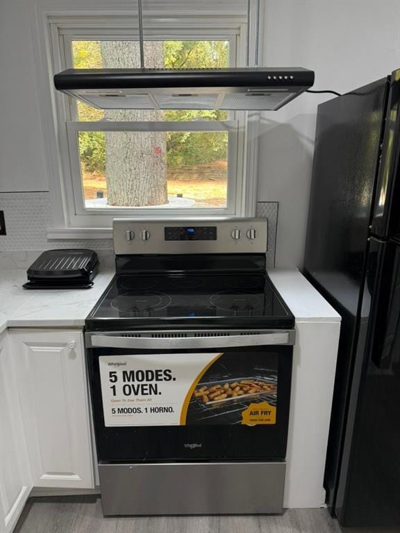 kitchen featuring black refrigerator, white cabinetry, electric range, and a wealth of natural light