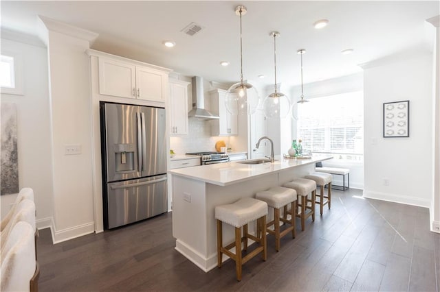 kitchen featuring a center island with sink, stainless steel appliances, light countertops, white cabinetry, and wall chimney exhaust hood