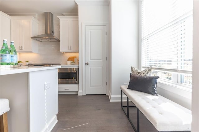 kitchen featuring tasteful backsplash, wall chimney exhaust hood, dark wood-type flooring, light countertops, and white cabinetry