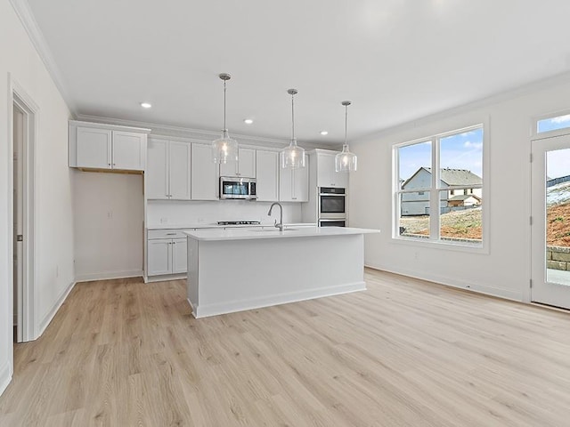 kitchen featuring decorative light fixtures, white cabinetry, appliances with stainless steel finishes, and a kitchen island with sink