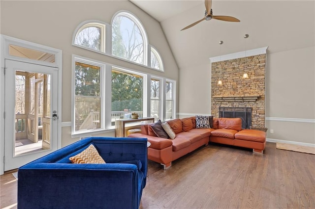 living room with ceiling fan, high vaulted ceiling, a stone fireplace, and hardwood / wood-style floors