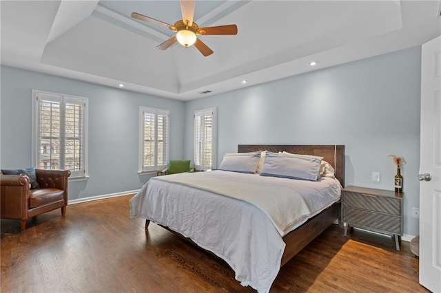 bedroom with dark hardwood / wood-style floors, a raised ceiling, and multiple windows