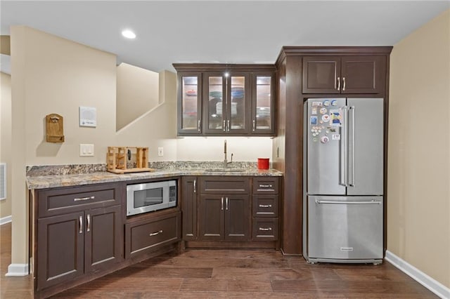 bar with light stone counters, sink, dark brown cabinets, and appliances with stainless steel finishes