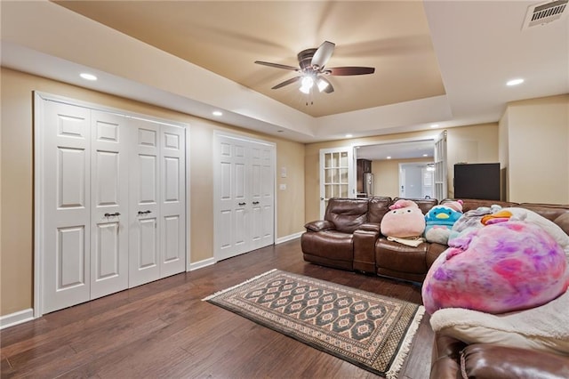 living room with hardwood / wood-style flooring, a raised ceiling, ceiling fan, and wood walls