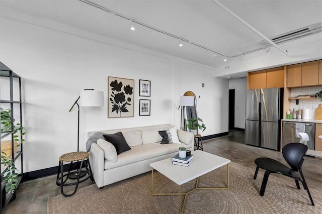 living room with concrete flooring, baseboards, and rail lighting