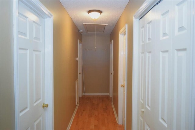 corridor with a textured ceiling and light hardwood / wood-style flooring