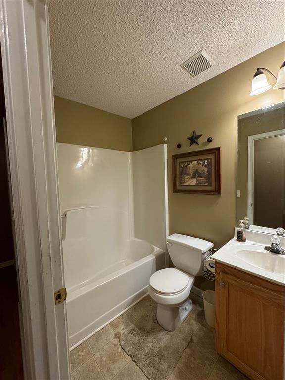 full bathroom with washtub / shower combination, vanity, a textured ceiling, and toilet