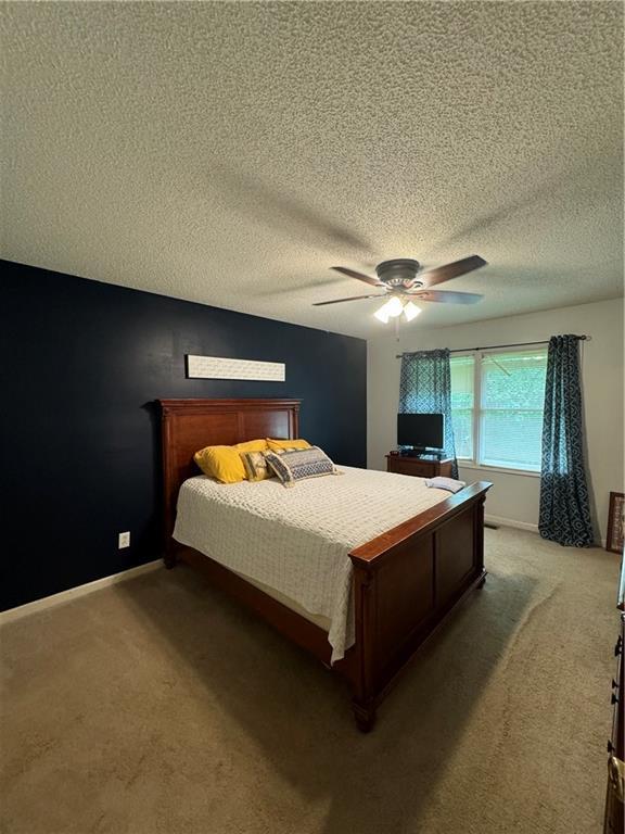 carpeted bedroom featuring ceiling fan and a textured ceiling