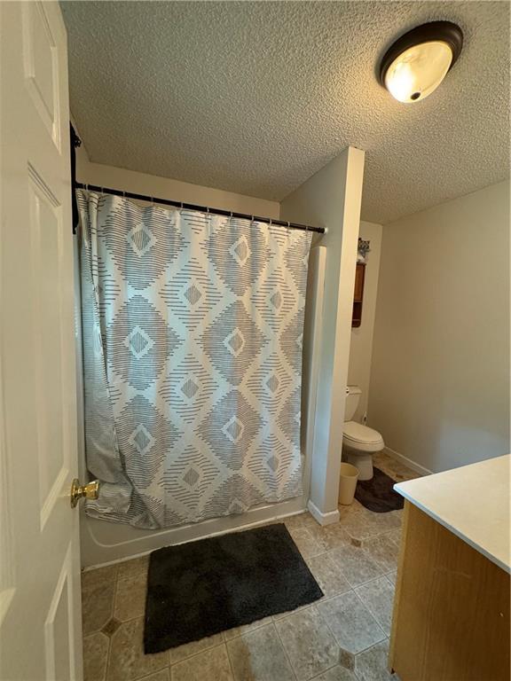 full bathroom featuring vanity, toilet, shower / bath combo with shower curtain, and a textured ceiling