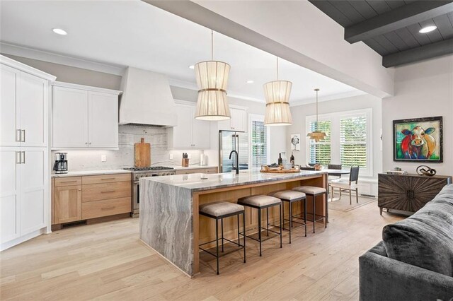 2583 Apple Valley Rd, Brookhaven, GA 30319 - kitchen with custom exhaust hood, stainless steel stove, light wood finished floors, a breakfast bar area, and decorative backsplash
