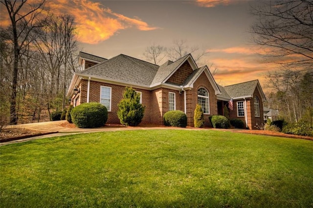 view of front of property with a shingled roof, brick siding, and a yard