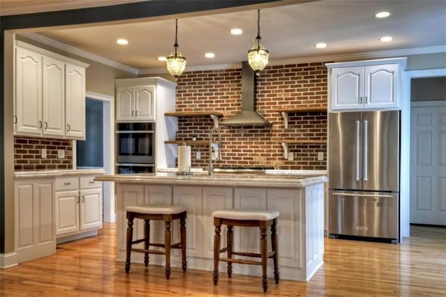 kitchen featuring appliances with stainless steel finishes, an island with sink, light wood-type flooring, and wall chimney range hood