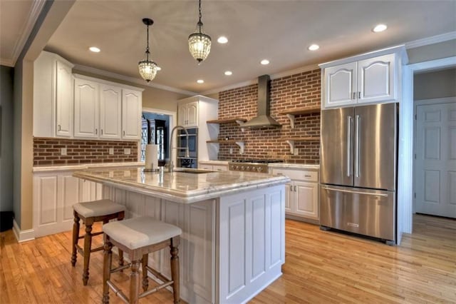 kitchen featuring light wood-style flooring, white cabinetry, appliances with stainless steel finishes, wall chimney exhaust hood, and pendant lighting