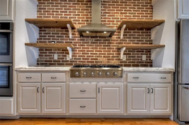 kitchen with wall chimney exhaust hood, stainless steel appliances, open shelves, and light countertops