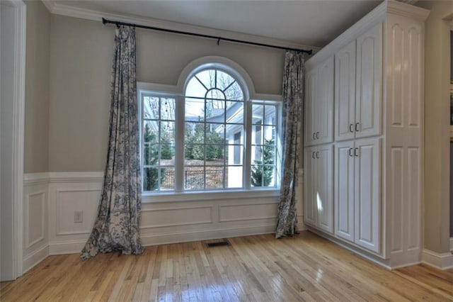 spare room with a wainscoted wall, visible vents, a decorative wall, and light wood-style flooring