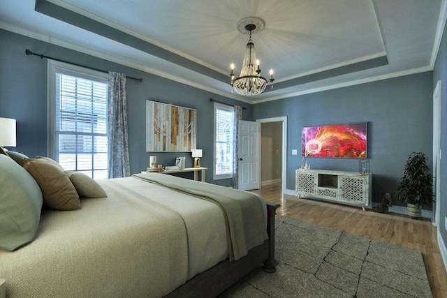 bedroom featuring ornamental molding, wood finished floors, a raised ceiling, and an inviting chandelier