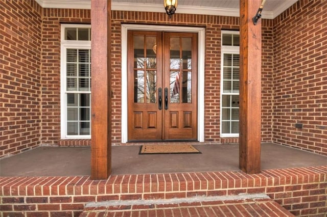 entrance to property featuring a porch, french doors, and brick siding