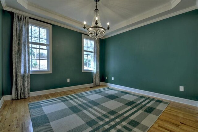 unfurnished room with a chandelier, a tray ceiling, wood finished floors, and crown molding