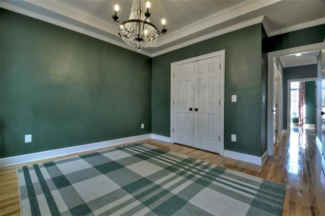 unfurnished bedroom featuring baseboards, wood finished floors, an inviting chandelier, a tray ceiling, and crown molding