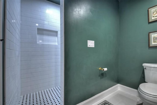 full bath with toilet, baseboards, and a tile shower