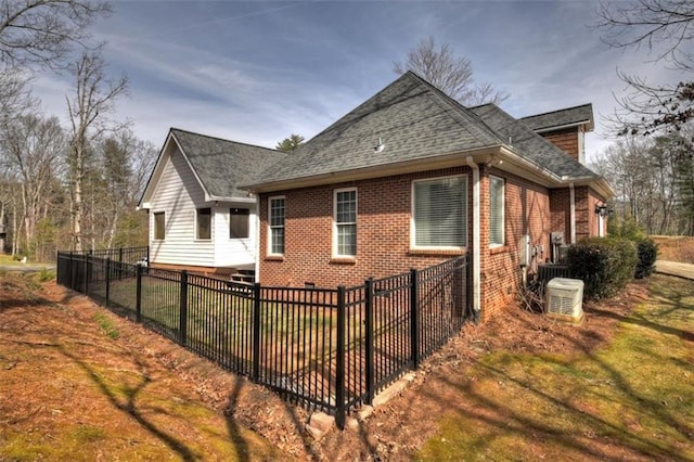 view of home's exterior with brick siding, fence, a lawn, and roof with shingles