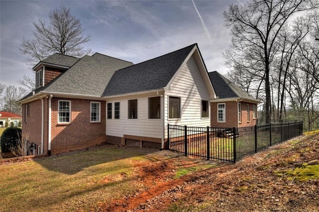 view of side of home with a yard, brick siding, fence, and a shingled roof