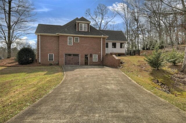 view of front of house featuring an attached garage, driveway, brick siding, and a front yard