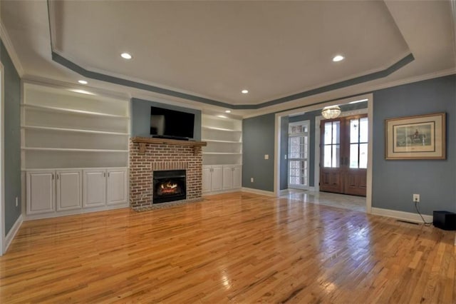 unfurnished living room with light wood-style floors, a fireplace, a tray ceiling, and crown molding