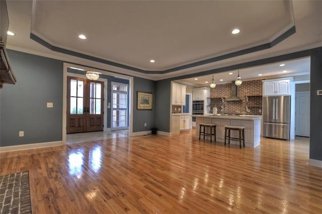 unfurnished living room with a raised ceiling, light wood-style flooring, and french doors