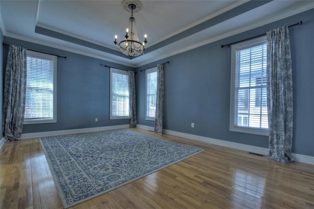 empty room featuring a healthy amount of sunlight, a tray ceiling, a notable chandelier, and ornamental molding