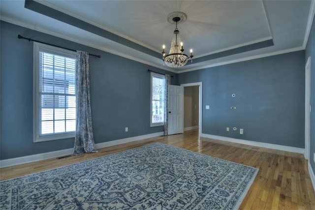 empty room with a wealth of natural light, a tray ceiling, crown molding, and wood finished floors