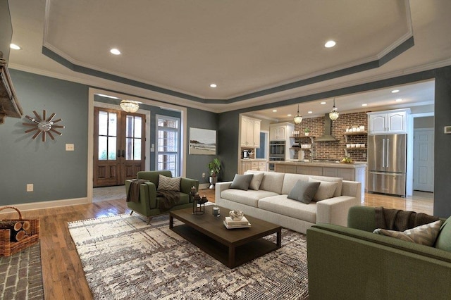 living room featuring light wood finished floors, baseboards, a raised ceiling, and recessed lighting