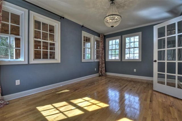 spare room with hardwood / wood-style flooring, baseboards, ornamental molding, and an inviting chandelier