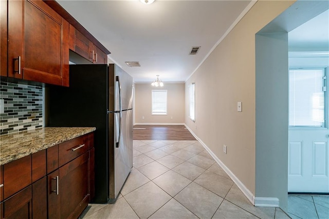 kitchen featuring light stone counters, crown molding, light tile patterned floors, stainless steel fridge, and backsplash