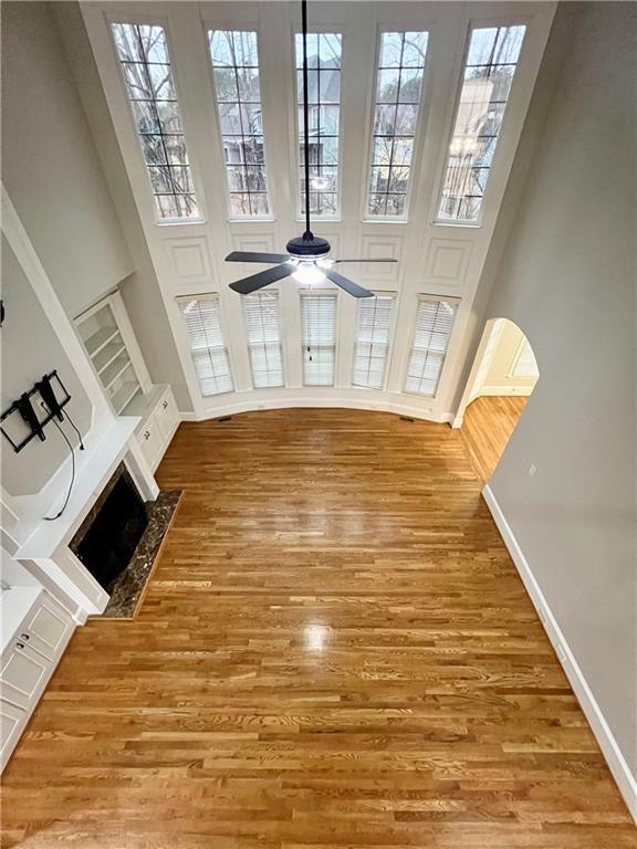 unfurnished living room featuring ceiling fan, a wealth of natural light, wood-type flooring, and a high ceiling