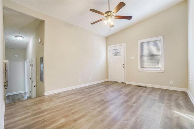 empty room featuring ceiling fan, light hardwood / wood-style floors, vaulted ceiling, and a textured ceiling